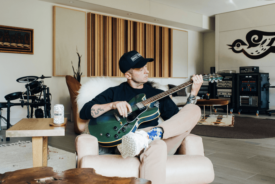 Musician playing guitar in a home studio, a can of Mad Tasty on the table beside him