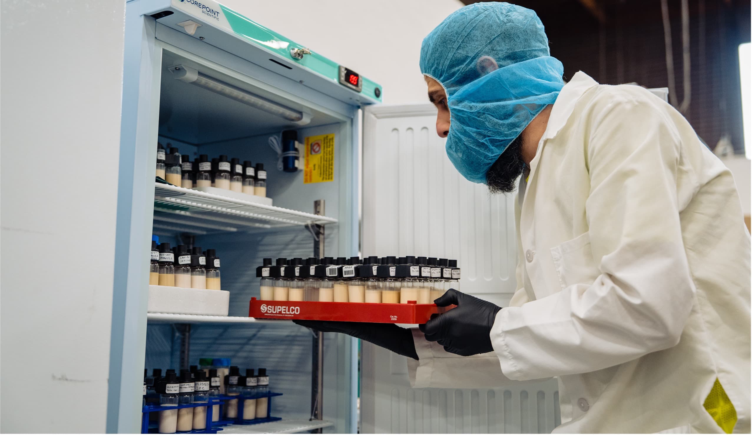 SōRSE scientist placing a rack of sample bottles into a stability-testing refrigerator