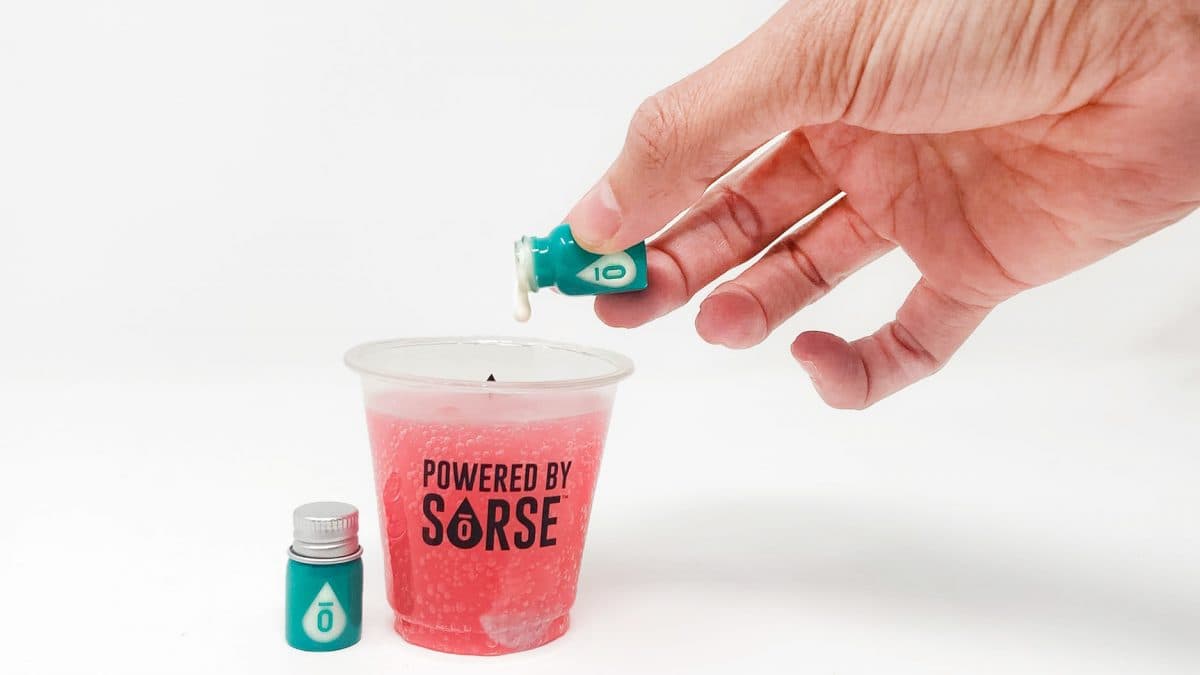 A hand adding SōRSE from a small teal bottle into a red drink in a Powered by SōRSE cup