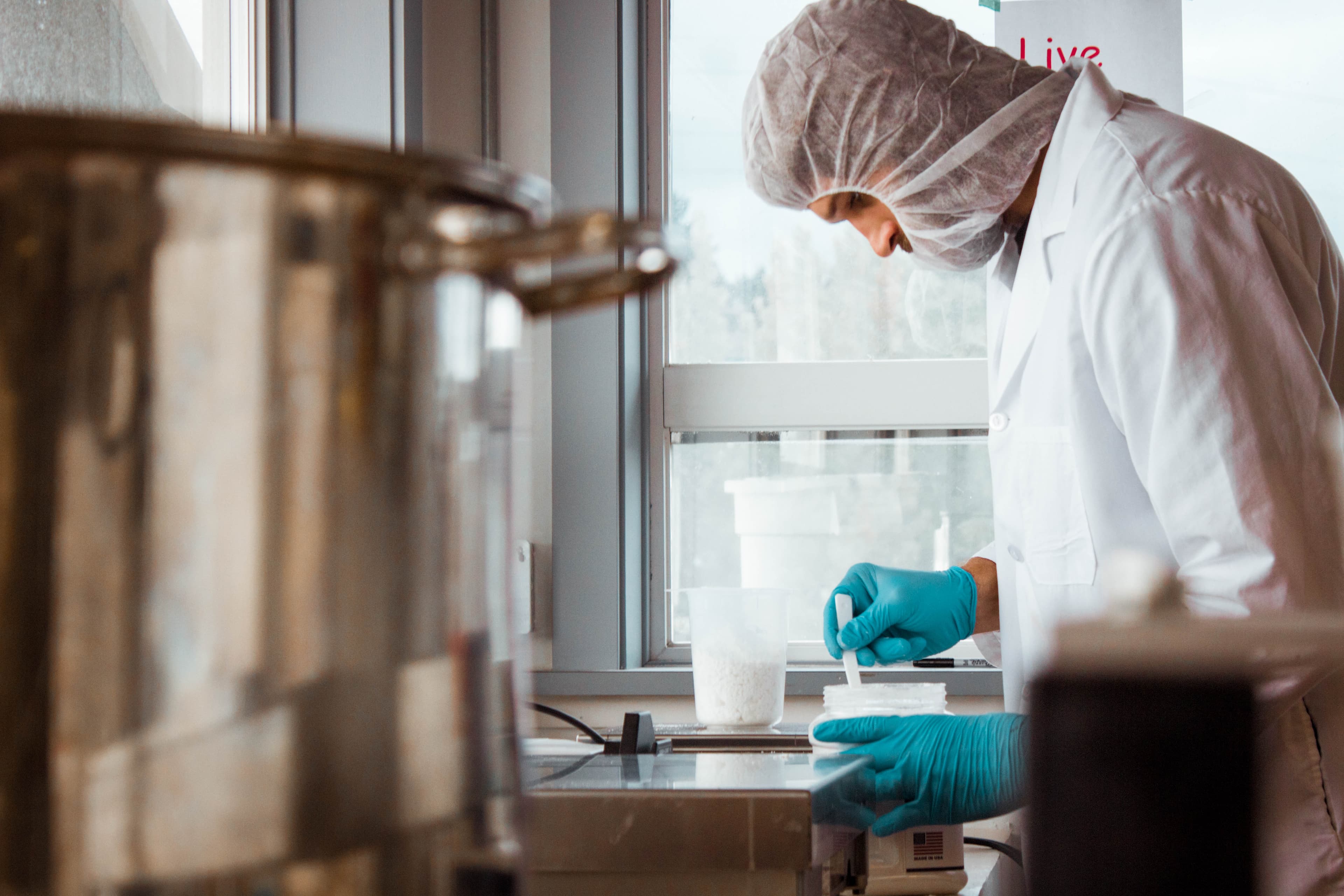 SōRSE scientist in a hairnet and gloves measuring ingredients at a lab bench