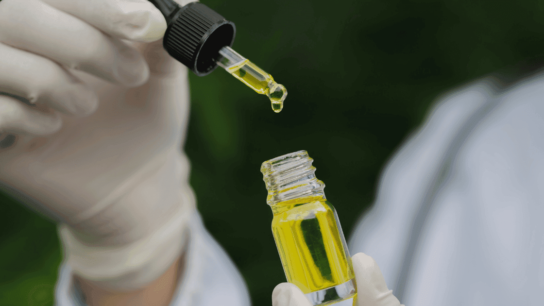 A gloved hand releasing a drop of golden SōRSE liquid from a dropper into a small glass bottle