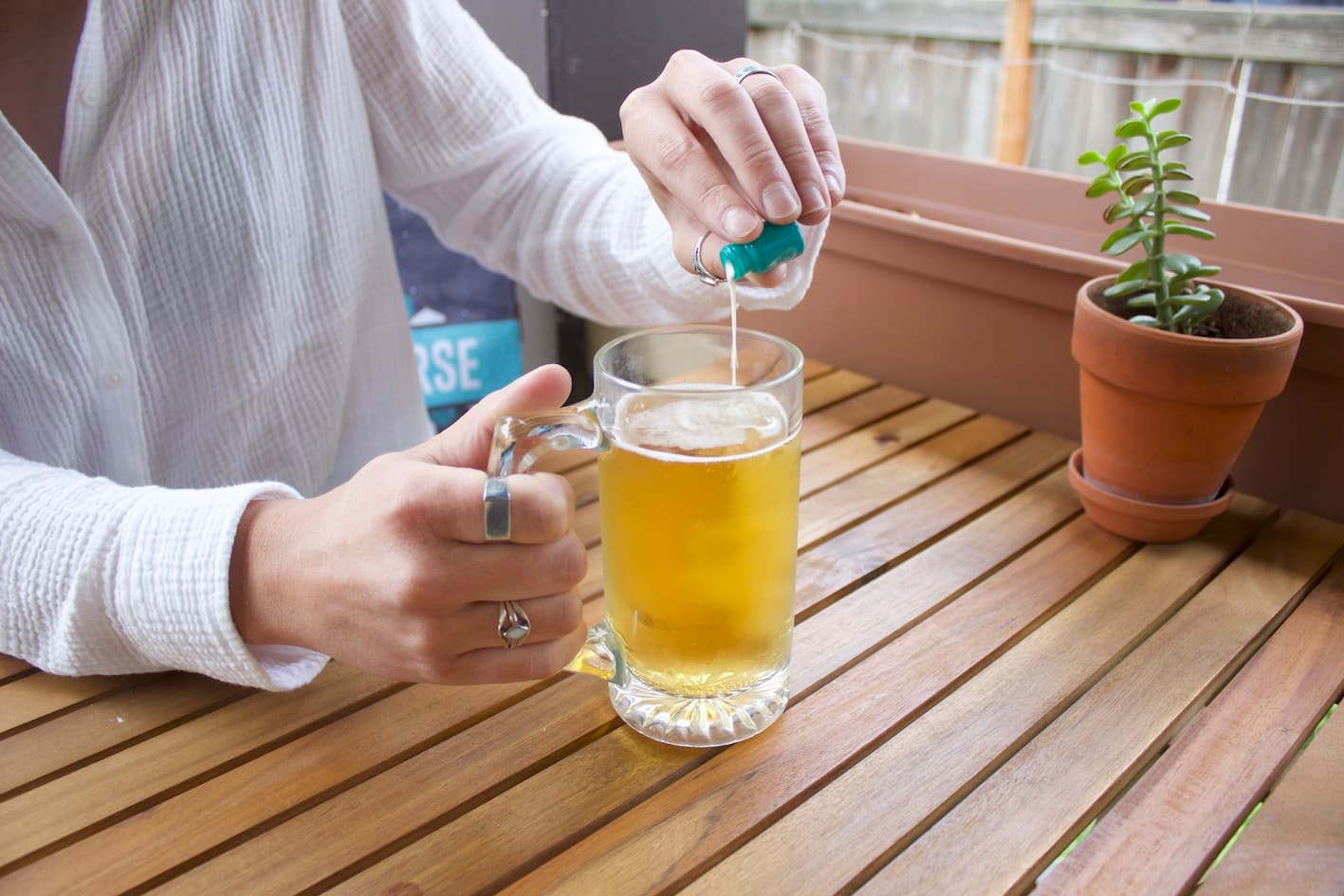 A hand squeezing a dropper of liquid into a mug of beer
